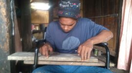 Reza sedang melukis nama di atas papan kayu untuk selanjutnya di pahatnya walaupun di atas kursi roda (Foto: Chen Rasi/Savanaparadise.com)
